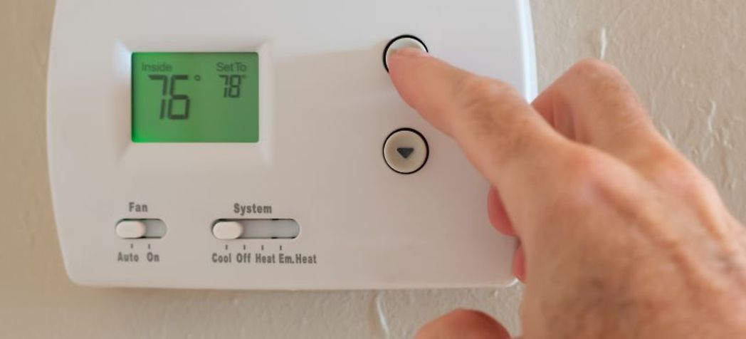 White thermostat with someone pressing buttons on the side - How to Program a Trane Thermostat
