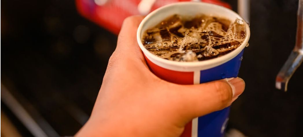 Hand holding a cup of soda next to beverage dispenser - Multiplex preventative maintenance & cleaning