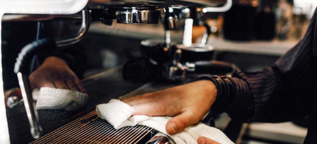 Mans hand wiping down espresso machine with a white towel - Sanremo espresso machine cleaning tips